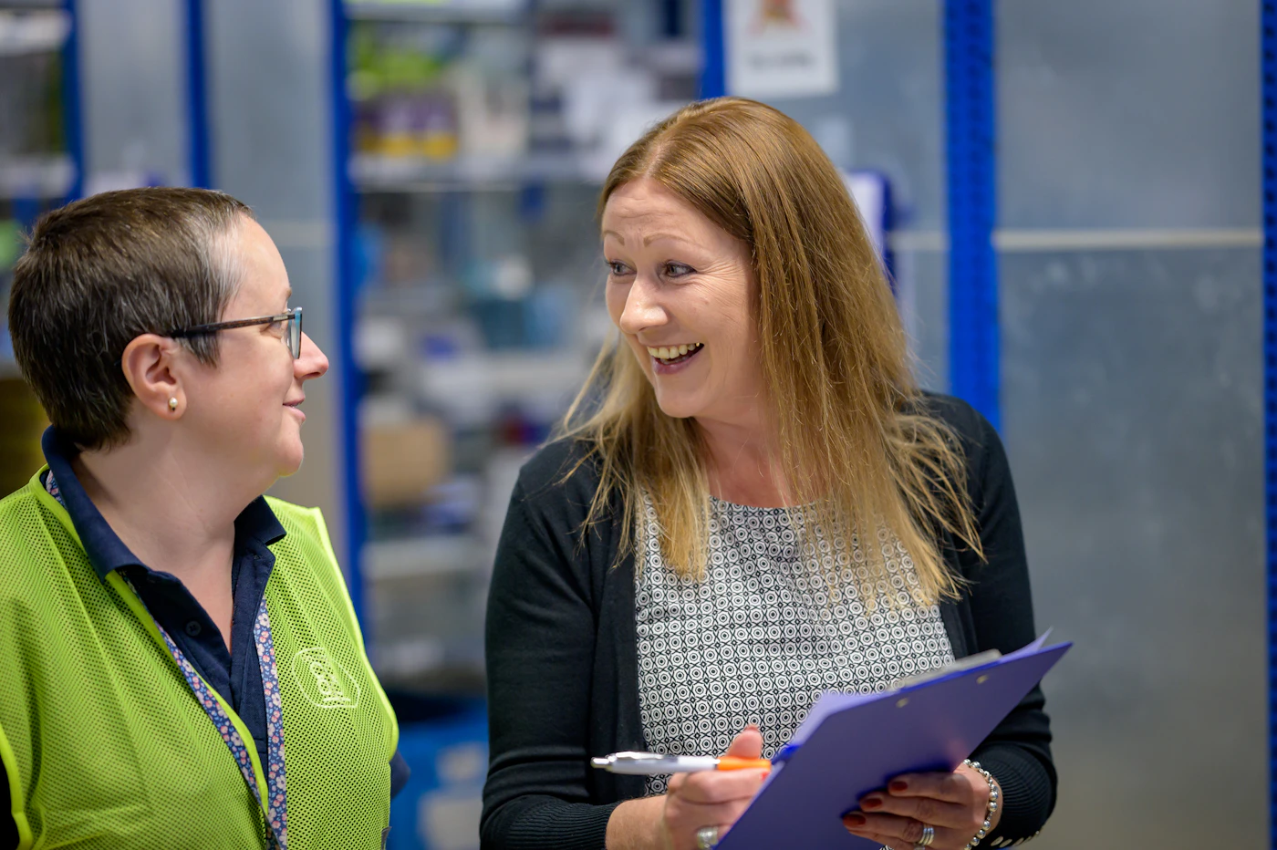 A warehouse manager with a clipboard talking with a team lead